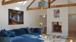 A living room with a blue sofa, a fireplace, a painting, and a ceiling with wooden beams.