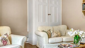 A living room with a white sofa, a matching armchair, a wooden coffee table, and a white door in the background. - 1 bedroom accommodation in Hollesley, near Woodbridge (Hollesley, near Woodbridge)