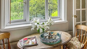 A room with a window overlooking a lush green landscape, a table with a magazine, a tray with tea set, and a chair with a floral cushion. - 1 bedroom accommodation in Hollesley, near Woodbridge (Hollesley, near Woodbridge)