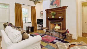 Una sala de estar con chimenea, un sofá, un televisor y un ventanal con cortinas.