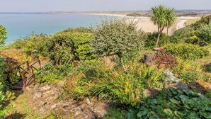 Paesaggio costiero con vegetazione variegata, spiaggia sabbiosa e vista limpida sul mare.