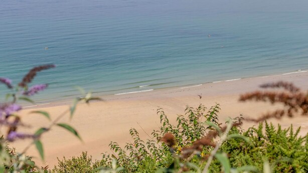 Paesaggio costiero con spiaggia, mare calmo e colline sullo sfondo.