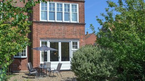 A two-story brick building with a patio area featuring a table and chairs, and a large umbrella. - 2 bedroom accommodation in Sheringham (Sheringham)