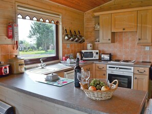 A kitchen with wooden cabinets, a sink, a microwave, a toaster, and a window with a view of greenery. - Hartland Forest Golf & Leisure (Woolsery, near Bideford)