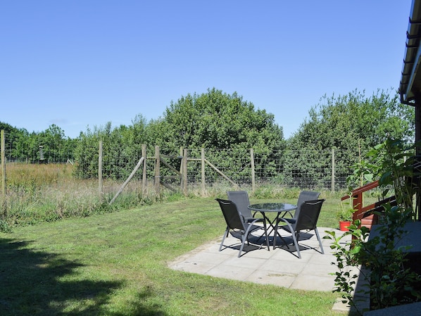 Une terrasse extérieure avec une table et des chaises, entourée d’une pelouse et d’une clôture en bois.