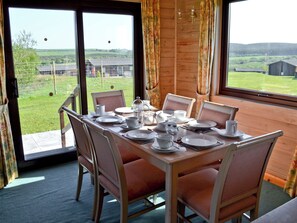 Een eetgedeelte met een tafel gedekt voor vier personen, stoelen en uitzicht op het landschap door grote ramen.