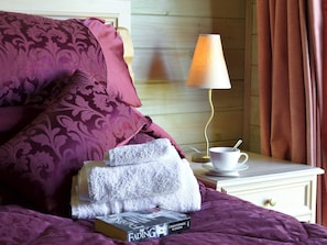 Un lit bien fait, recouvert d’une couverture et de coussins violets, une table de chevet blanche avec une tasse et une soucoupe, et un livre intitulé « Le Déclin ».