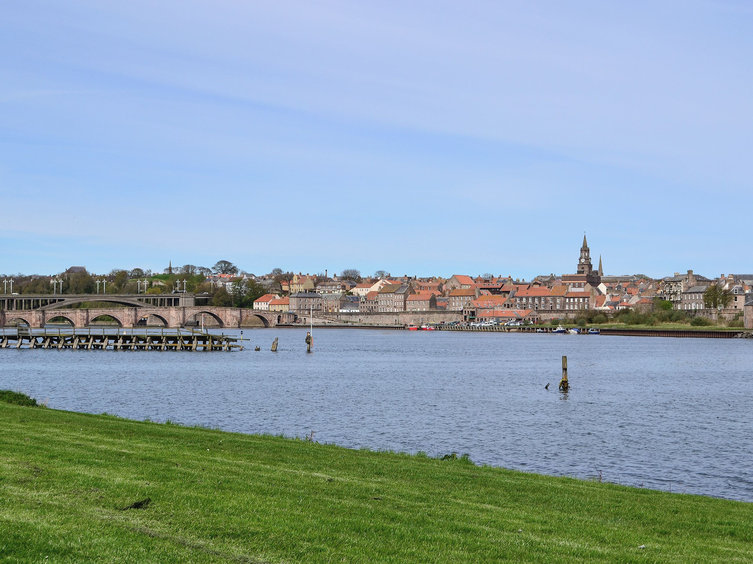En utsikt över en stad från flodstranden, med historiska byggnader, en bro och ett kyrktorn.