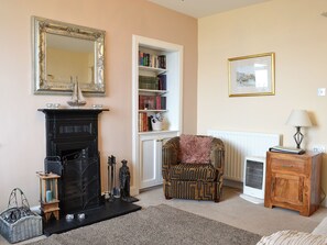 A living room with a fireplace, a bookshelf, a patterned armchair, a wooden cabinet, and a framed picture on the wall.