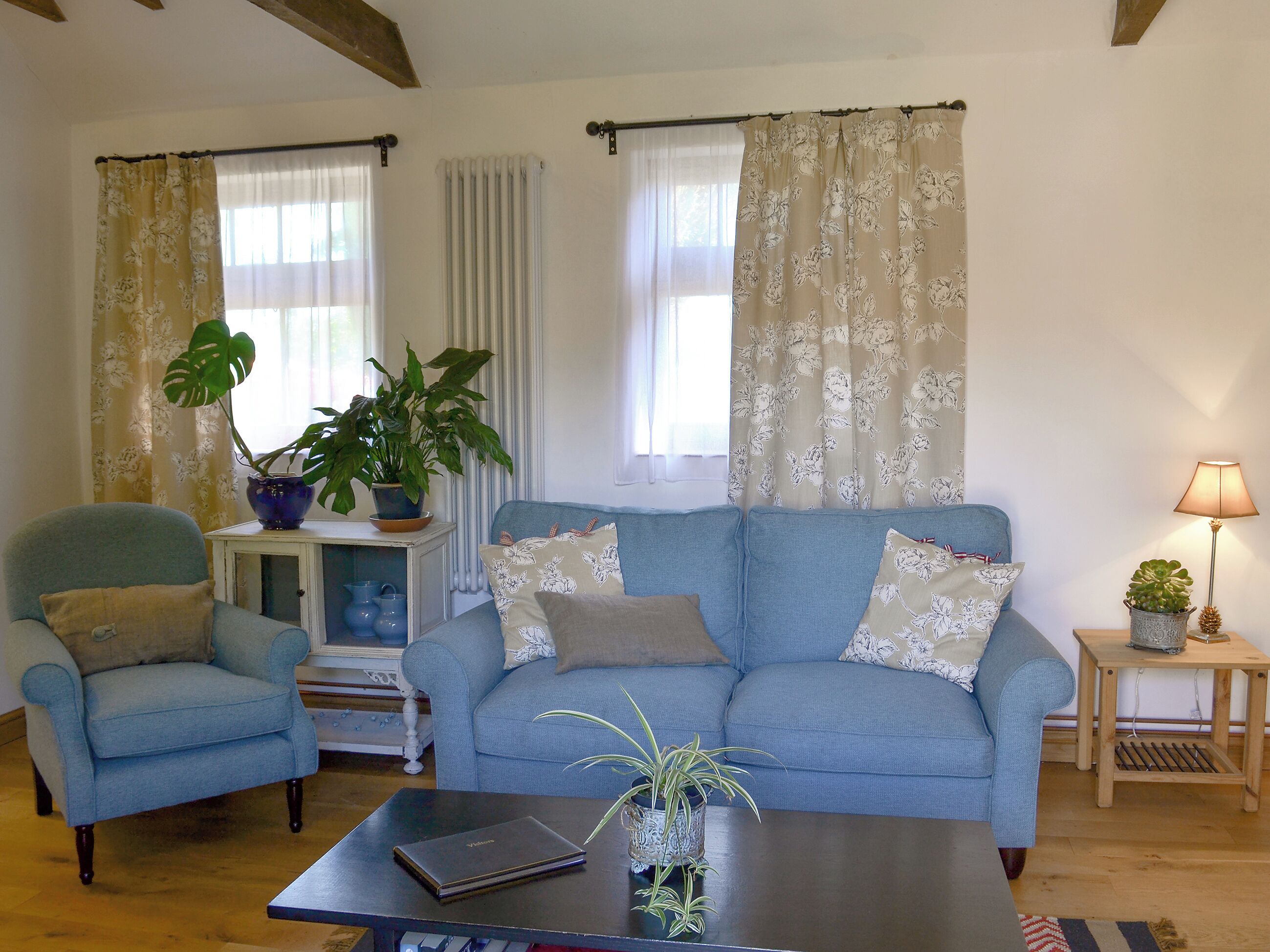 Ein Wohnzimmer mit einem blauen Sofa, einem blauen Sessel, einem kleinen Tisch mit einem Laptop und einer Lampe auf einem Beistelltisch.