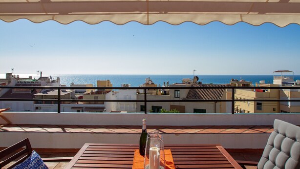 Une terrasse avec vue sur la mer, une bouteille de champagne et un verre posé sur une table.
