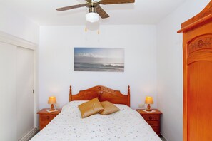 A bedroom with a wooden bed, two bedside lamps, a ceiling fan, and a wall-mounted picture of a beach. - Silvia | Rooftop Terrace, Sea View & Beach (Torremolinos)