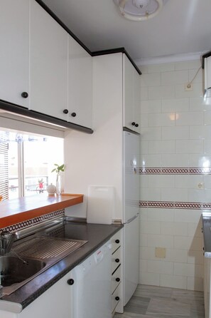 A compact kitchen with white cabinets, a stainless steel sink, and a window with blinds. - Silvia | Rooftop Terrace, Sea View & Beach (Torremolinos)