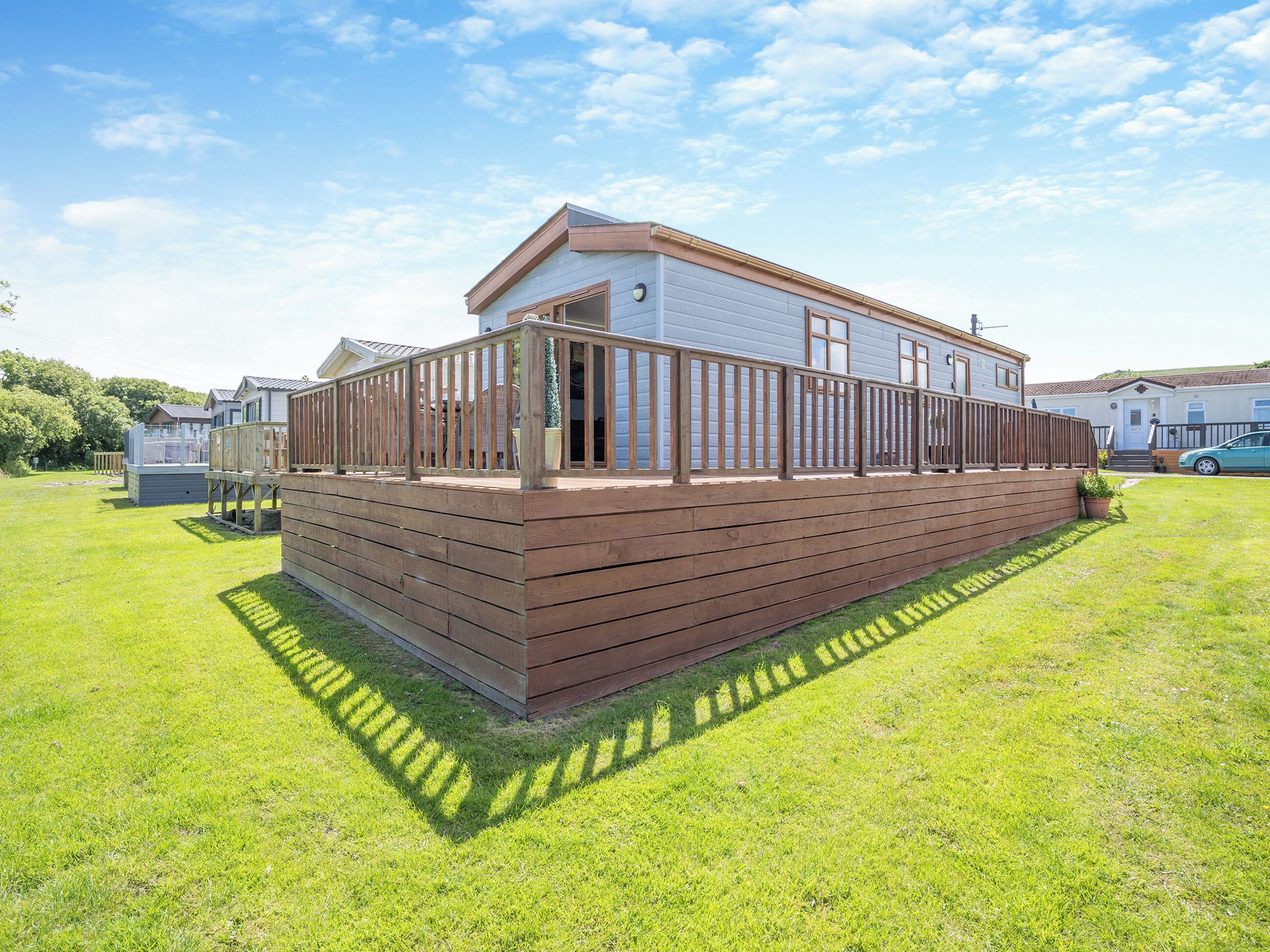 A single-story mobile home with a wooden deck and a fenced patio area.