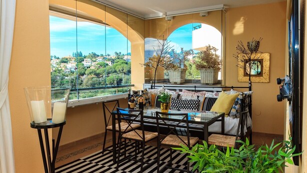 Un balcón con mesa y sillas, plantas en macetas y vistas a un barrio residencial.