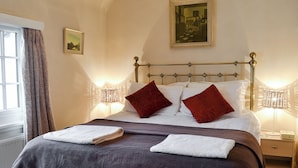 A neatly made bed with two white towels, a dark brown bedspread, and two red pillows. There is a framed picture on the wall above the bed, a window with curtains, and a bedside table with a lamp. - 2 bedroom accommodation in Llanddona, near Beaumaris (Llanddona, near Beaumaris)