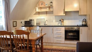 A kitchen with wooden cabinets, a microwave, a kettle, and a dining table with chairs. - 2 bedroom accommodation in Llanddona, near Beaumaris (Llanddona, near Beaumaris)