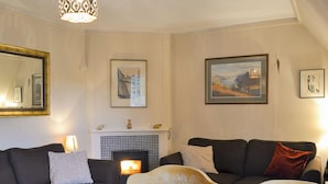 A living room with two dark sofas, a wooden table, a fireplace, and framed artwork on the walls. - 2 bedroom accommodation in Llanddona, near Beaumaris (Llanddona, near Beaumaris)