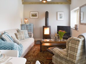 A cozy living room with a sofa, a plaid armchair, a coffee table, a fireplace, and a television.