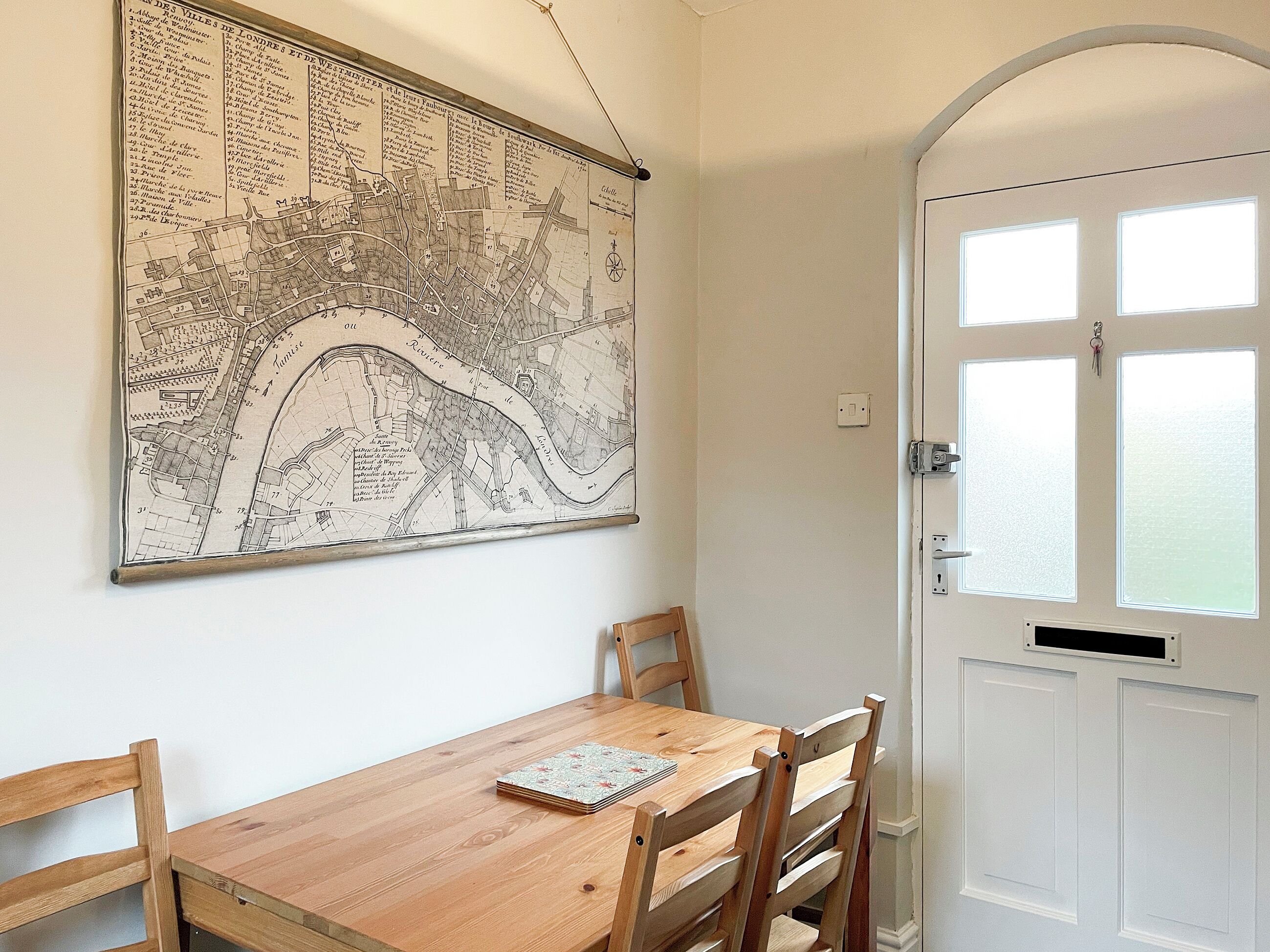 Een eettafel met stoelen, een kaart aan de muur en een witte deur met ramen.