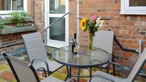 A round glass table with metal chairs, a bottle of wine, and a vase of flowers.