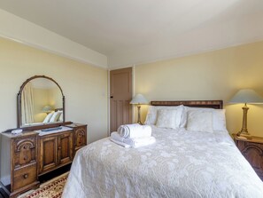 Una habitación de hotel con una cama grande, dos lámparas de noche, un aparador de madera y un espejo.