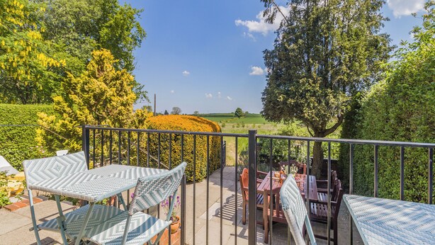 A balcony with a view of a field, a table with chairs, and a potted plant. - Bryn Tor - The Gardener's House (Bolsover, near Chesterfield)