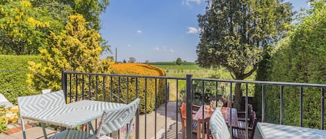 A balcony with a view of a field, a table with chairs, and a potted plant.