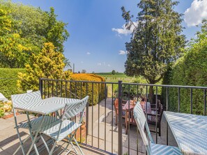 A balcony with a view of a field, a table with chairs, and a potted plant.