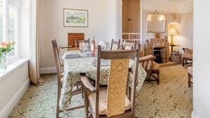 A dining area with a table set for four, surrounded by wooden chairs with cushioned seats. A framed landscape painting hangs on the wall above the table.