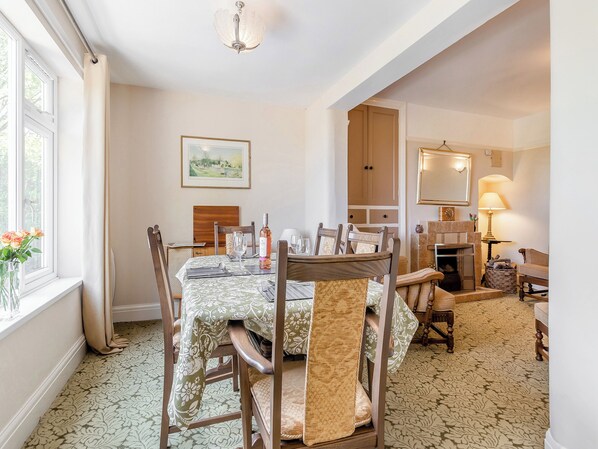 Un comedor con una mesa dispuesta para cuatro personas, rodeada de sillas de madera con asientos acolchados. Un cuadro enmarcado de un paisaje cuelga en la pared sobre la mesa.