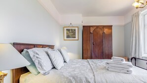 A neatly made bed with a floral-patterned bedspread and pillows, a wooden wardrobe, and a framed picture on the wall.