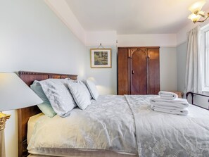 Een net opgemaakt bed met een bloemenprint sprei en kussens, een houten garderobe en een lijst met een foto aan de muur.