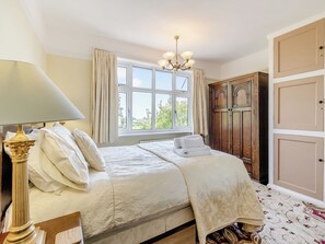A bedroom with a large bed, a chandelier, a window with curtains, and a wardrobe.