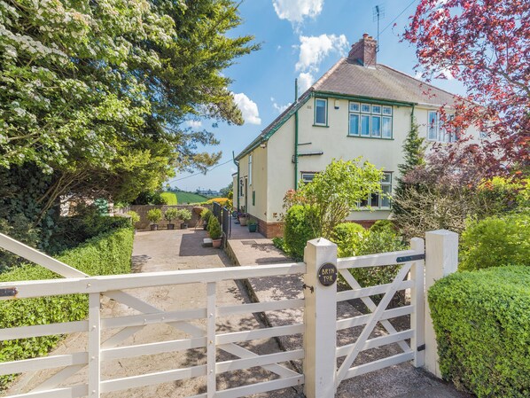 A gated entrance to a house with a garden, a paved pathway, and a clear sky.