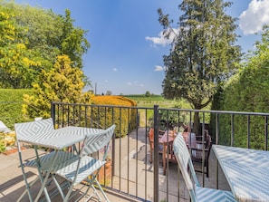 Een balkon met uitzicht op een veld, een tafel met stoelen en een bloempot.