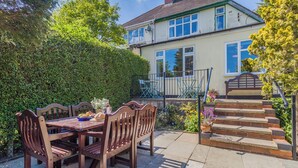 A patio with a wooden table and chairs, a small garden, and a two-story house with a visible staircase.