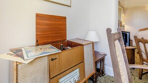 A room with a wooden cabinet, a small table with a lamp, a chair, and a framed picture on the wall. - Bryn Tor - The Gardener's House (Bolsover, near Chesterfield)