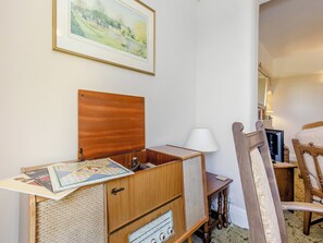 A room with a wooden cabinet, a small table with a lamp, a chair, and a framed picture on the wall. - Bryn Tor - The Gardener's House (Bolsover, near Chesterfield)