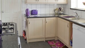 A kitchen with light-colored cabinets, a gas stove, a sink, and a window with a flower arrangement.