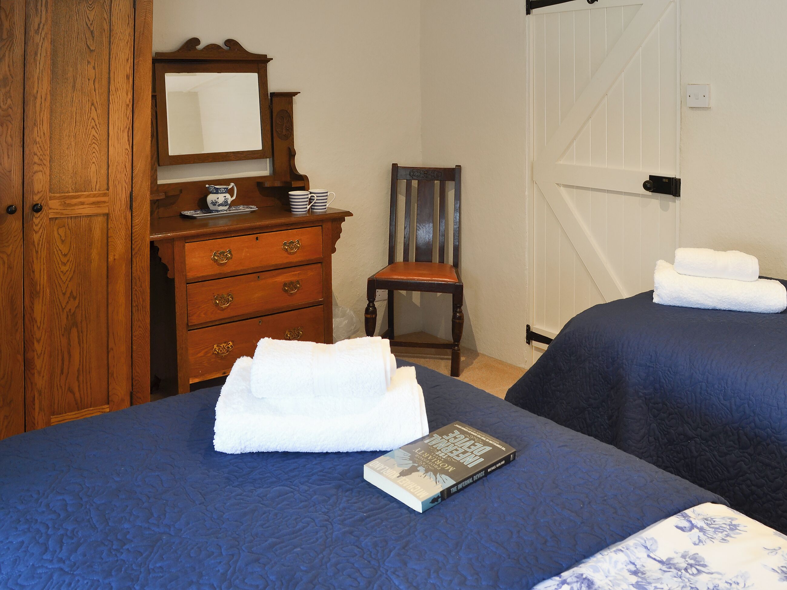 Une chambre avec deux lits, une commode en bois, une chaise et un livre posé sur l’un des lits.