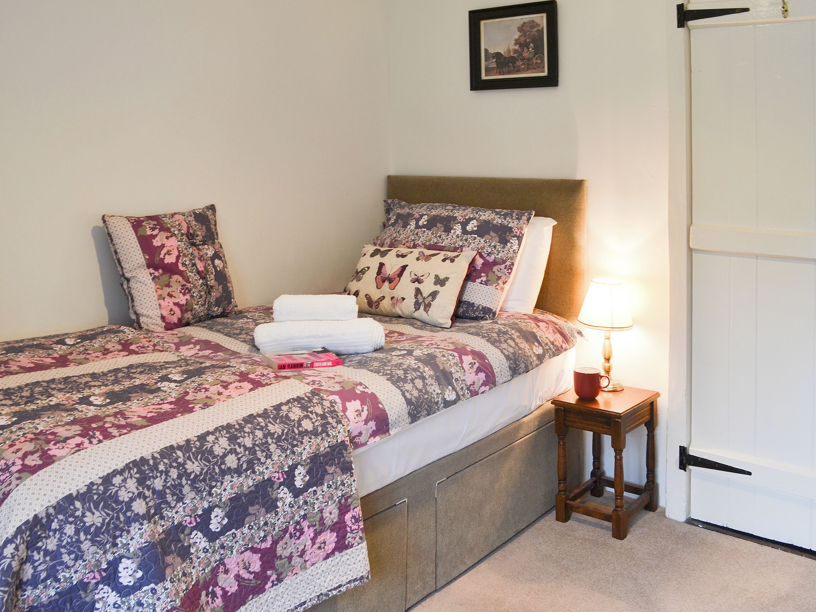 A neatly made bed with floral bedding, a bedside table with a lamp, and a framed picture on the wall.