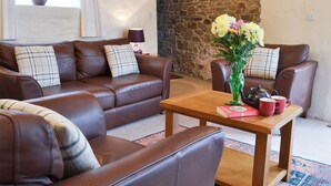 A cozy living room with a brown leather sofa, a wooden coffee table, and a stone wall. - 5 bedroom accommodation in Parkham, near Bideford (Parkham, near Bideford)