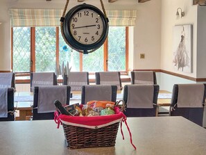 A dining area with a clock, chairs, a table, and a basket with snacks.