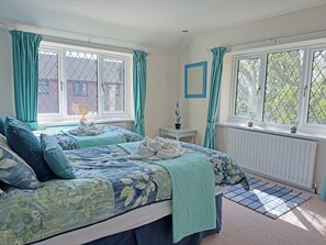 A bedroom with two beds, teal curtains, a radiator, and a view of a brick building.