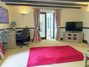 Una habitación con escritorio, silla, televisor, alfombra roja y vista por una puerta.