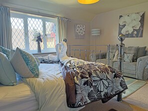 Un dormitorio con cama, ventana con cortinas, radiador, aire acondicionado instalado en la pared, sofá y un objeto decorativo en la pared.