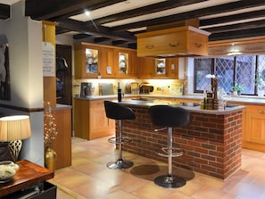 Una cocina con armarios de madera, una isla de ladrillo, dos taburetes de bar y una ventana con vistas.