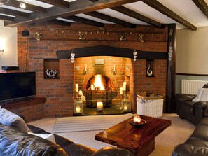 Una sala de estar acogedora con chimenea de ladrillo, sofás de cuero, una mesa de centro de madera y un televisor.