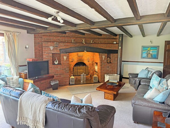 A living room with a brick fireplace, leather sofas, a flat-screen TV, and a wooden coffee table.